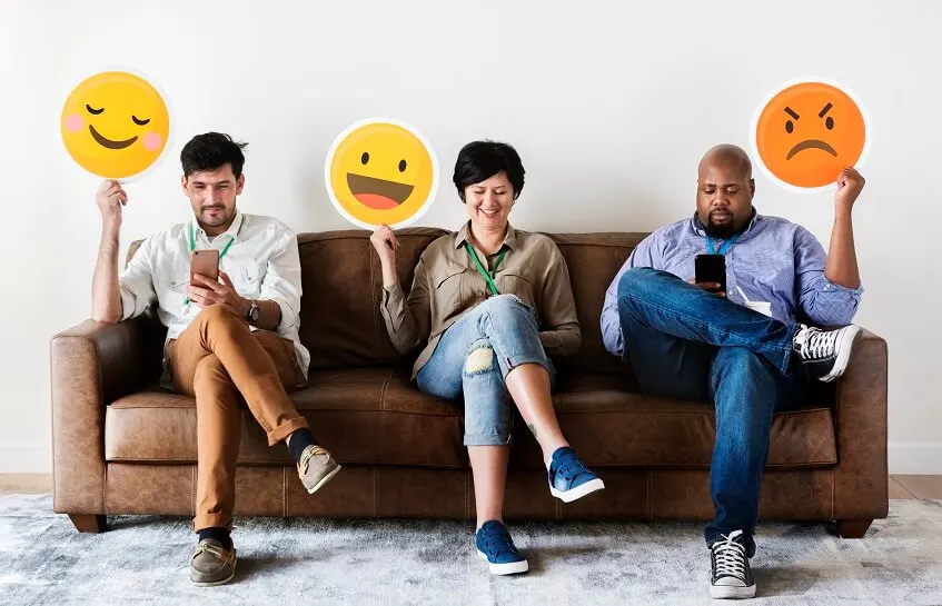 people on social media on smartphones holding different emojis to show their sentiment